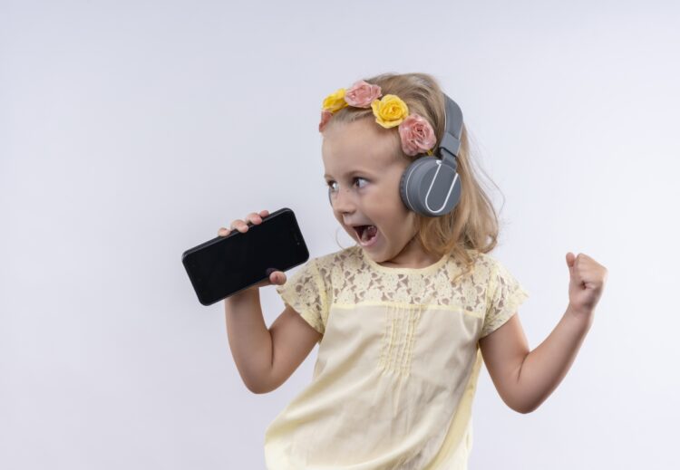 Baby Yoga: The Benefits and How to Get Started 68 Optimized cute little girl wearing yellow shirt floral headband listening singing from mobile phone with headphones white wall 1