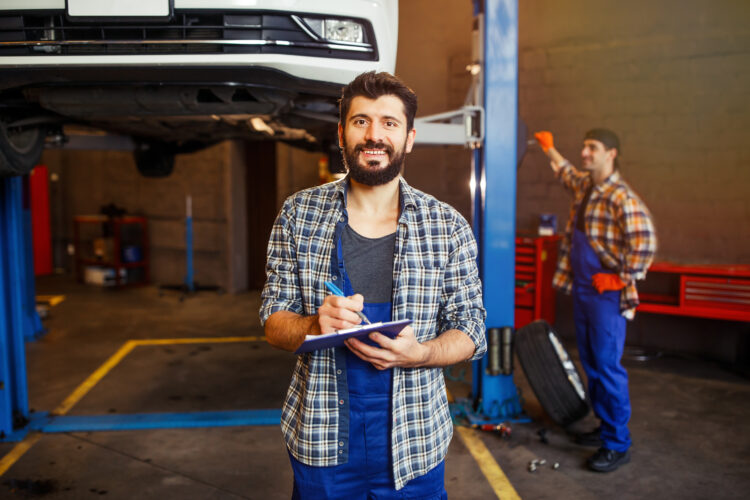 Garage Business 52 portrait young automechanic writing clipboard looking camera while another specialist working 1